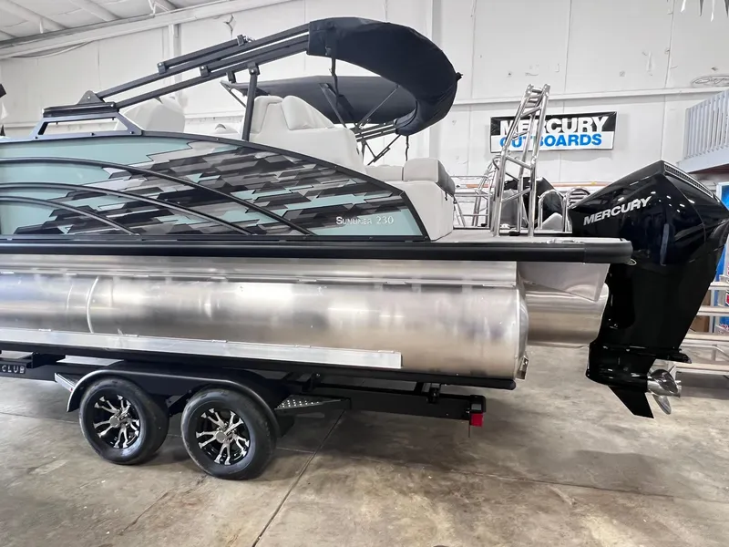Slide: The Image of 2024 Harris Sunliner 230 pontoon boat with Mercury outboard, displayed indoors on a trailer. - 3
