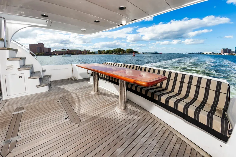 Slide: The Image of 2007 Hatteras 64 Motor Yacht deck with striped seating and wooden table, overlooking water. - 21