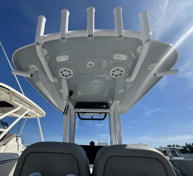 Slide: The Image of 2025 Sportsman Heritage 231 boat, T-top view with rod holders and speakers under clear sky. - 30