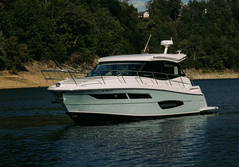 Slide: The Image of 2021 Regal 38 Grande Coupe yacht cruising on a serene lake with forested shoreline. - 1