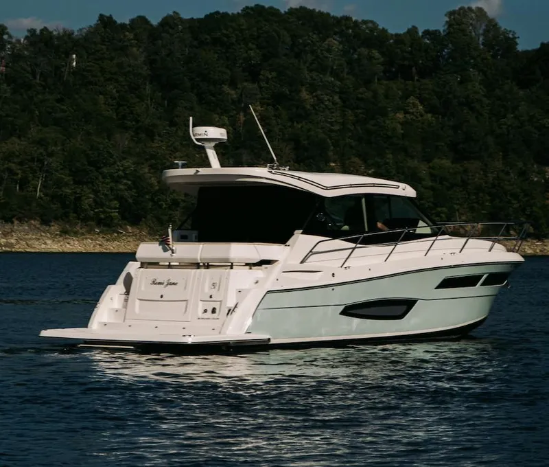 Slide: The Image of 2021 Regal 38 Grande Coupe yacht cruising on a serene lake with forested backdrop. - 4