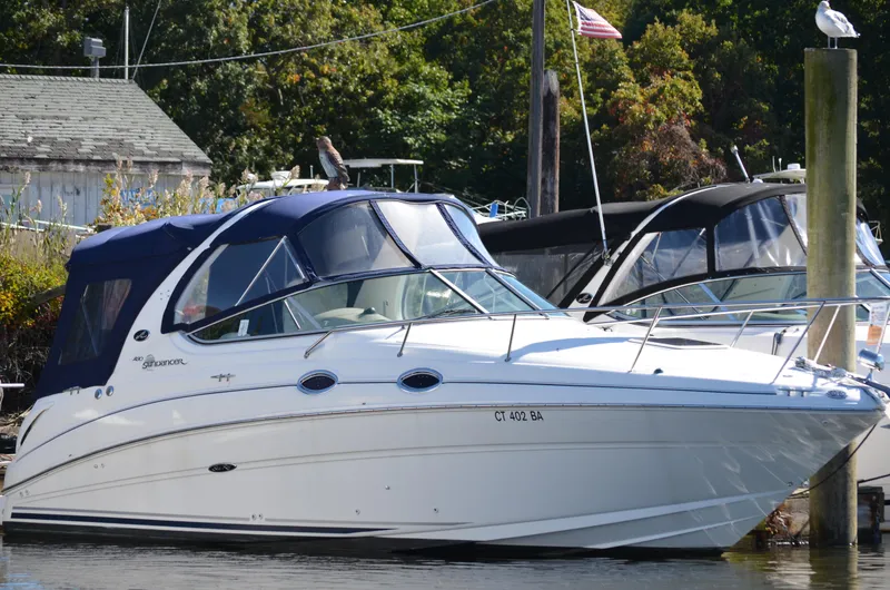Slide: The Image of 2004 Sea Ray 280 Sundancer docked, featuring blue canopy and sleek white hull. - 0
