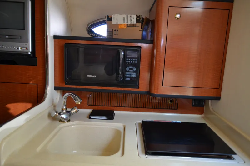 Slide: The Image of 2004 Sea Ray 280 Sundancer galley with microwave, sink, and wooden cabinetry. - 39