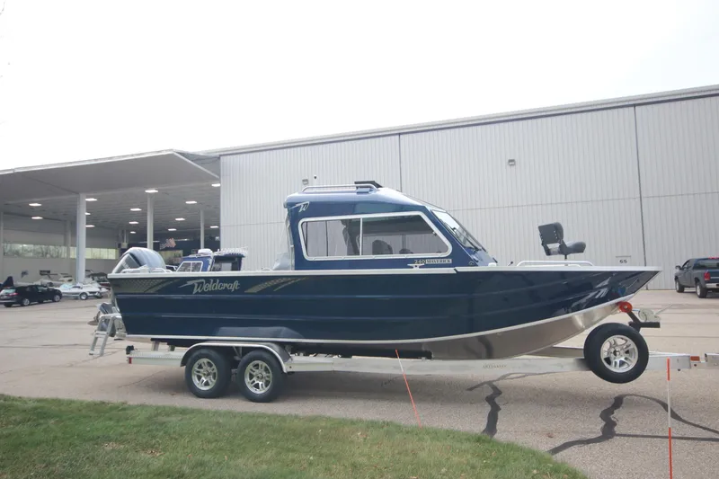Slide: The Image of 2025 Weldcraft 240 Maverick DV boat on trailer, parked outside a large building. - 4