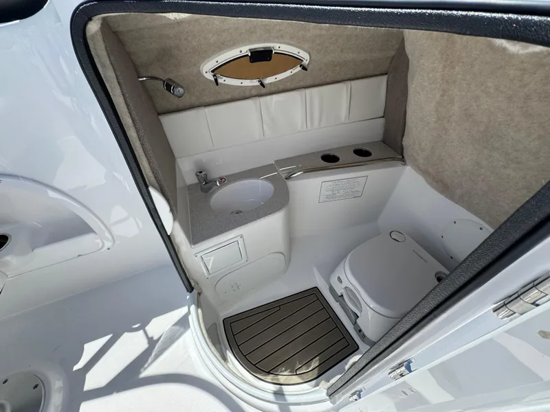 Slide: The Image of 2025 Stingray 231DC boat interior with compact bathroom, featuring sink, toilet, and porthole window. - 13