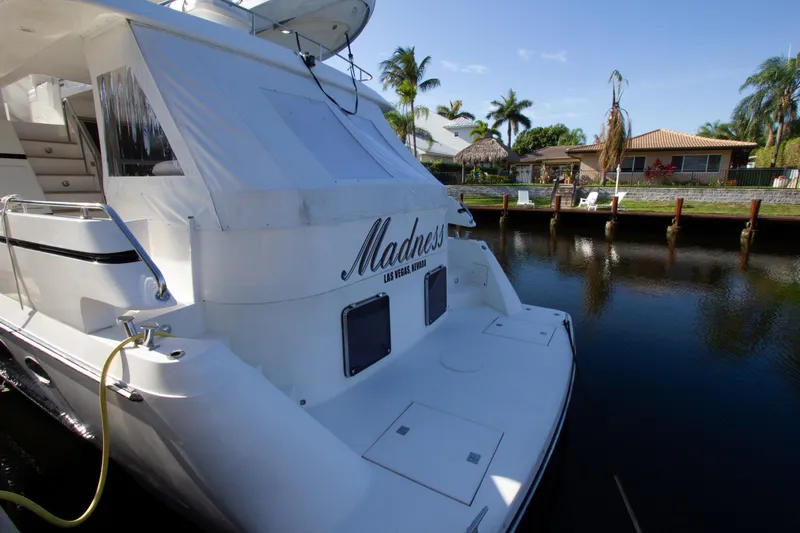 Slide: The Image of 1999 Johnson 70 Motor Yacht docked by waterfront homes, named "Madness." - 2