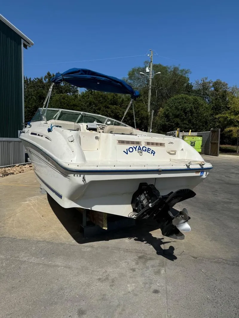 Slide: The Image of 1996 Sea Ray 215 Express Cruiser boat with blue canopy, named "Voyager," parked on concrete. - 6