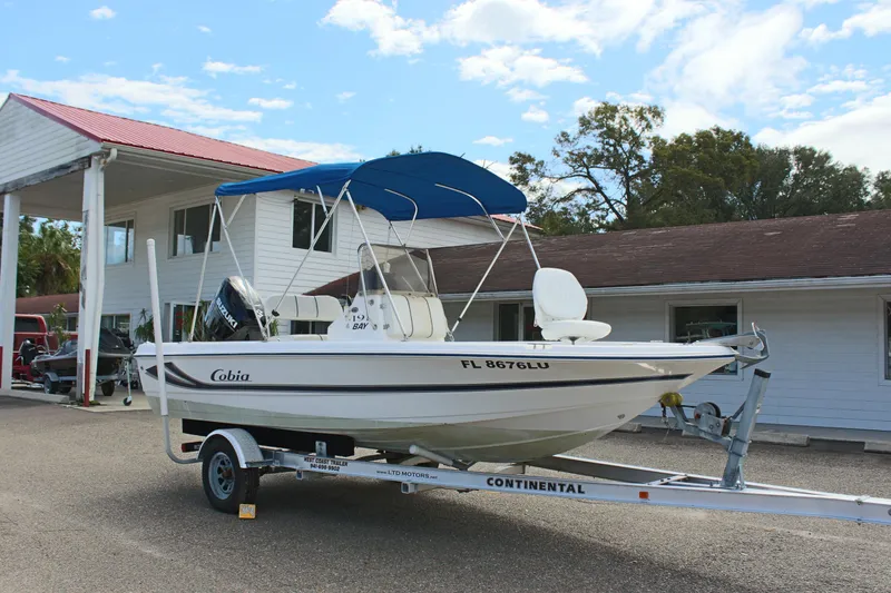 Slide: The Image of 2002 Cobia 191 Bay boat on trailer with blue canopy, parked near buildings. - 29