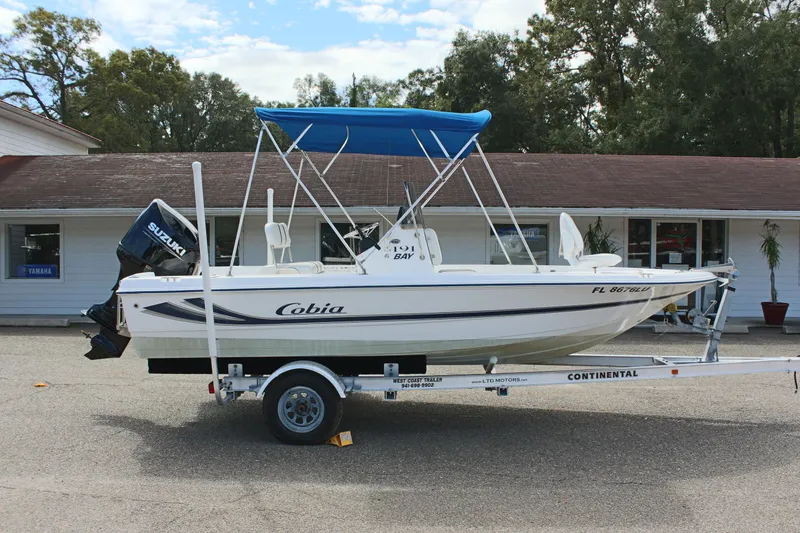 Slide: The Image of 2002 Cobia 191 Bay boat on trailer with blue canopy, parked outside a building. - 4