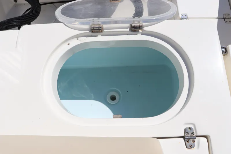 Slide: The Image of Open livewell on 2012 Cobia 256 CC boat, featuring a clear lid and white interior. - 17
