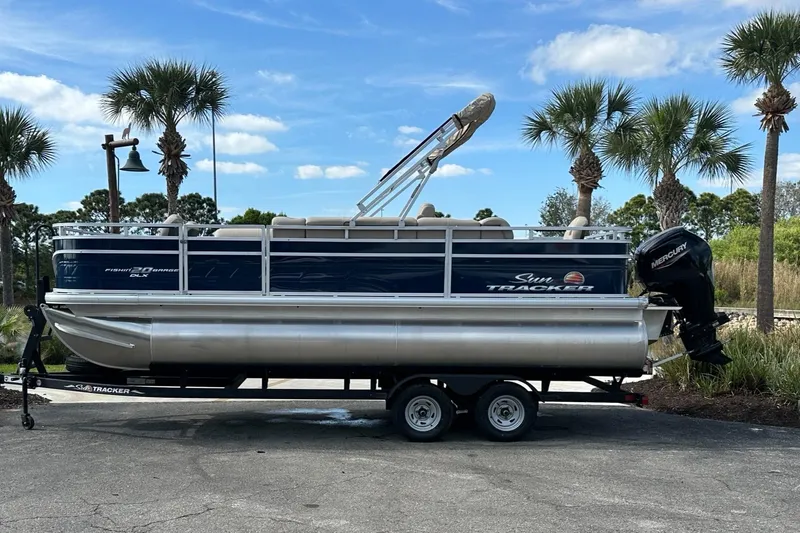 The Image of 2023 Sun Tracker Fishin' Barge 20 DLX pontoon boat on trailer, parked near palm trees. - 0