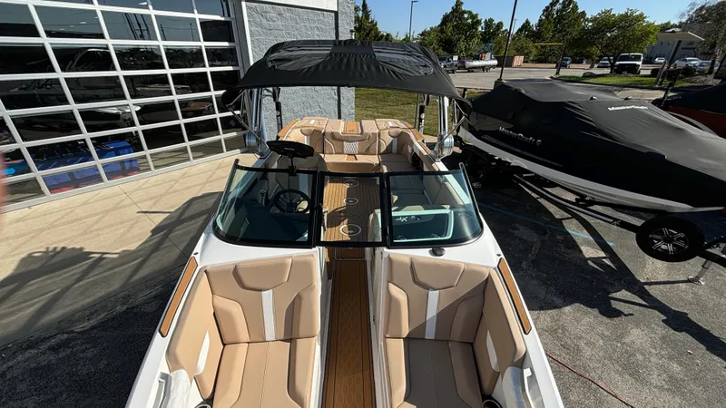 Slide: The Image of 2025 MasterCraft XT24 boat with tan seating and black canopy, parked outdoors. - 23