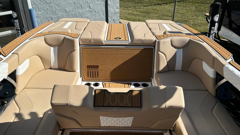 Slide: The Image of 2025 MasterCraft XT24 boat interior with beige and white seating, wood accents, and cup holders. - 33
