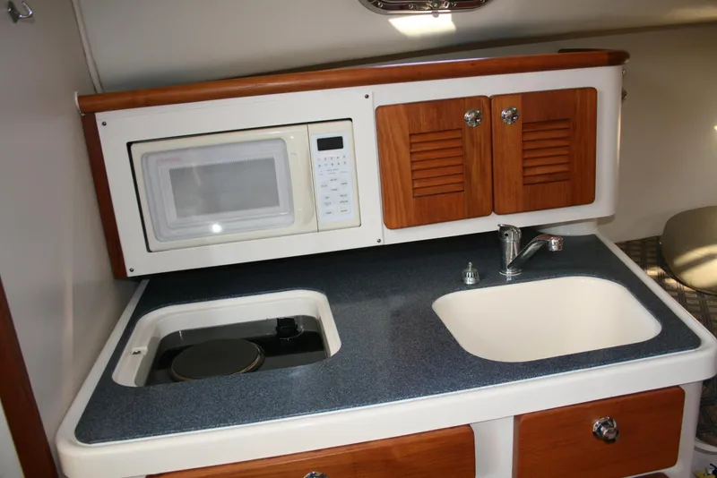 Slide: The Image of 2005 Pursuit 3370 Offshore boat kitchen with microwave, sink, and wooden cabinets. - 11