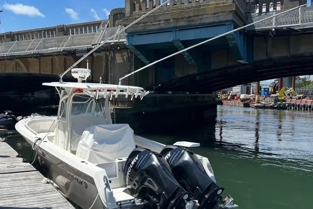 Slide: The Image of 2014 Sailfish 270 CC boat docked near a bridge, featuring dual outboard motors. - 2