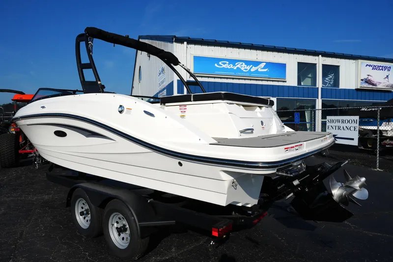 Slide: The Image of 2025 Sea Ray SPX 230 boat on trailer outside showroom, under clear blue sky. - 16