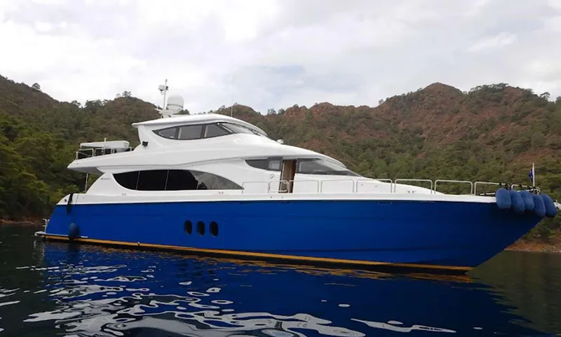 The Image of 2007 Hatteras Enclosed Flybridge yacht with blue hull, anchored near lush, forested hills. - 1
