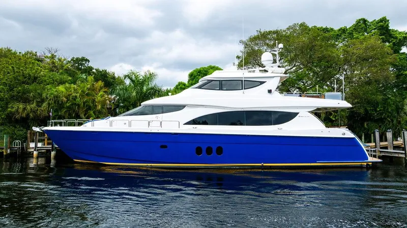 Slide: The Image of 2007 Hatteras Enclosed Flybridge yacht with blue hull docked by lush greenery. - 2