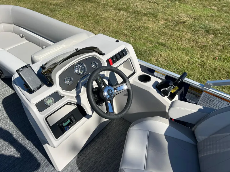 Slide: The Image of 2025 Godfrey Xperience 2286 SFL boat dashboard with steering wheel and controls, on grassy background. - 22