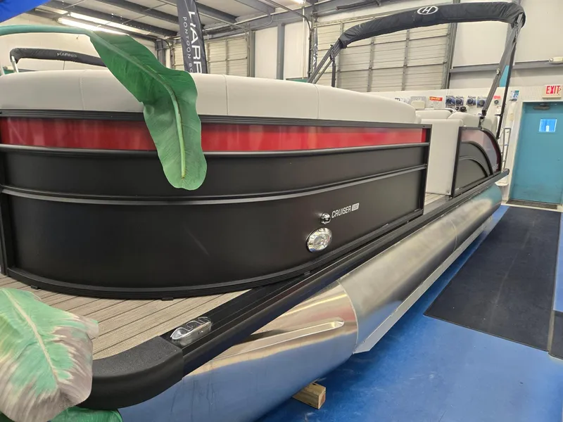 Slide: The Image of 2024 Harris Cruiser 230 pontoon boat displayed indoors, featuring sleek black and red design. - 2