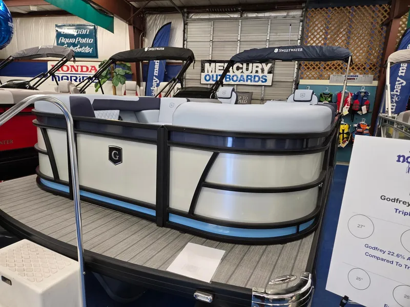 Slide: The Image of 2025 Godfrey SWEETWATER 2286 SFL pontoon boat displayed indoors with Mercury outboards signage. - 2