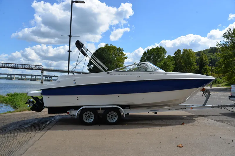 Slide: The Image of 2006 Bayliner 249 SD boat on trailer by river, under blue sky. - 15
