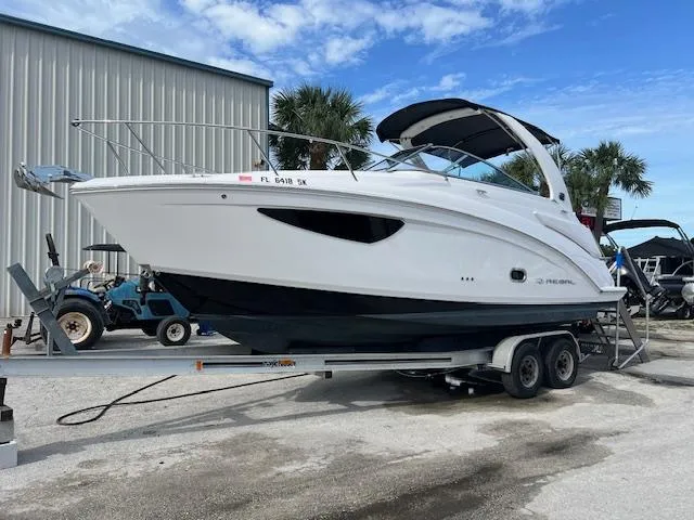 The Image of 2019 Regal 26 Express boat on trailer, parked outdoors near a warehouse. - 0
