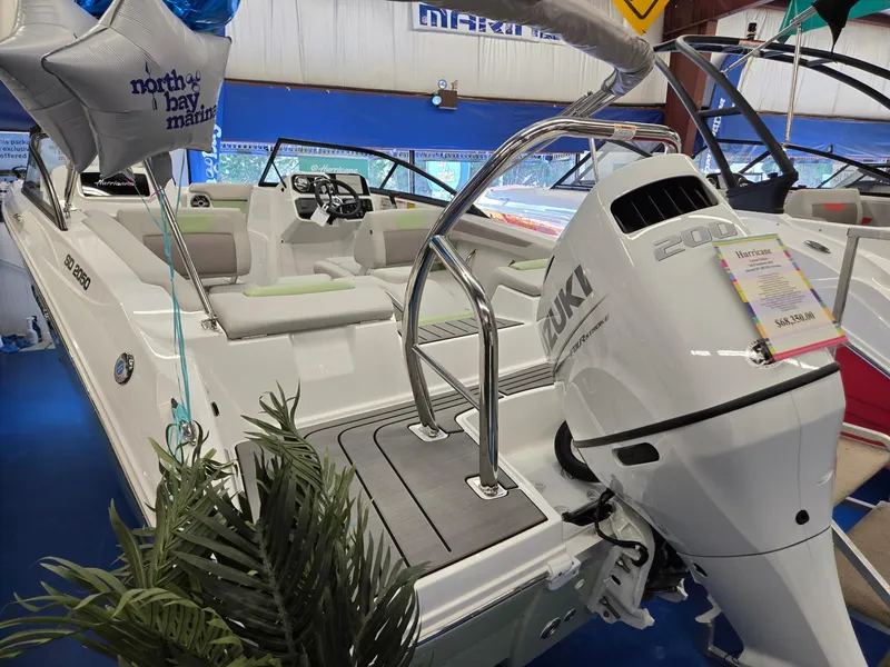 Slide: The Image of 2025 Hurricane SunDeck 2050 OB boat with Suzuki outboard motor on display indoors. - 2