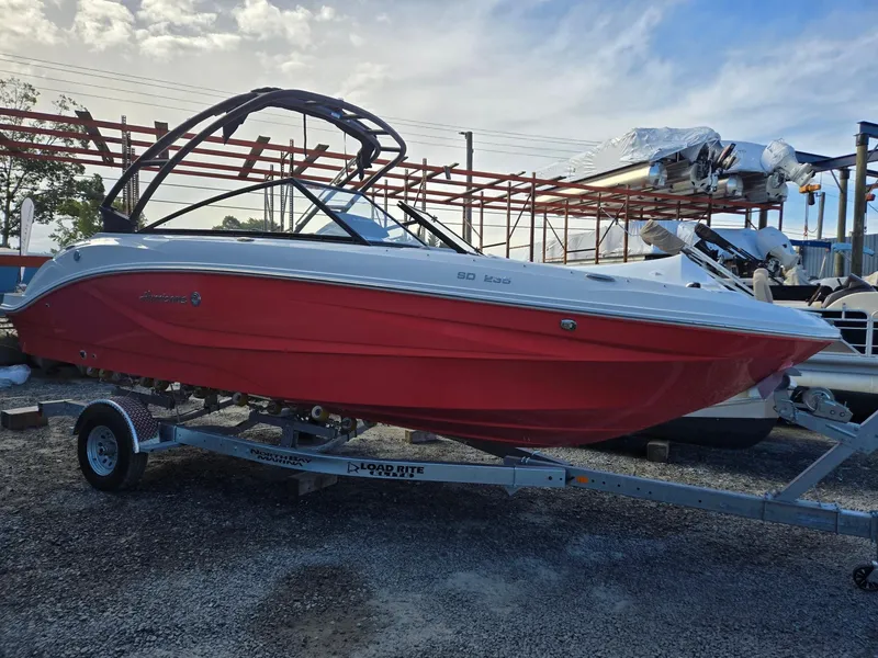 Slide: The Image of 2025 Hurricane SunDeck 235 OB boat with red hull on trailer, outdoor setting. - 2