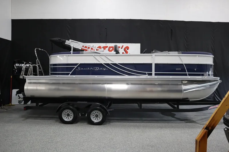 The Image of 2025 South Bay 222E pontoon boat on trailer in indoor showroom. - 0
