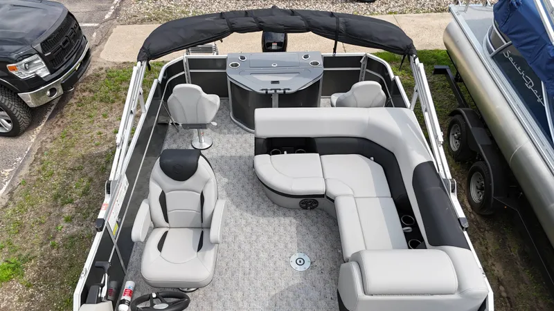 Slide: The Image of 2025 South Bay 220 F pontoon boat interior with seating and helm, docked beside a truck. - 9