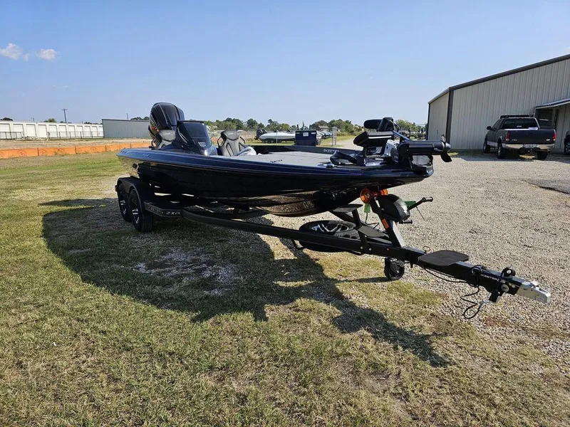 Slide: The Image of 2025 Skeeter ZXR19 boat on trailer parked on grass near a building. - 12