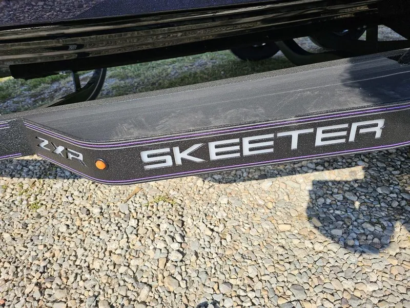 Slide: The Image of 2025 Skeeter ZXR19 boat trailer with logo on gravel surface. - 2