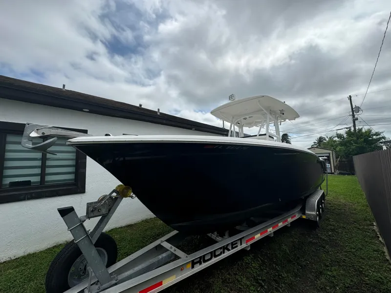 Slide: The Image of 2011 Sea Hunt Gamefish 29 boat on trailer, parked beside a house under cloudy skies. - 0