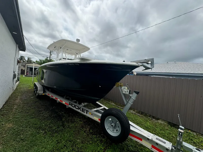 Slide: The Image of 2011 Sea Hunt Gamefish 29 boat on trailer, parked beside a building under cloudy skies. - 1