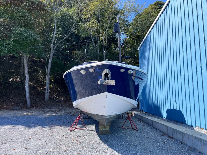 Slide: The Image of 2021 Cruisers Yachts 338 CX IO boat on stands, near blue building, surrounded by trees. - 3