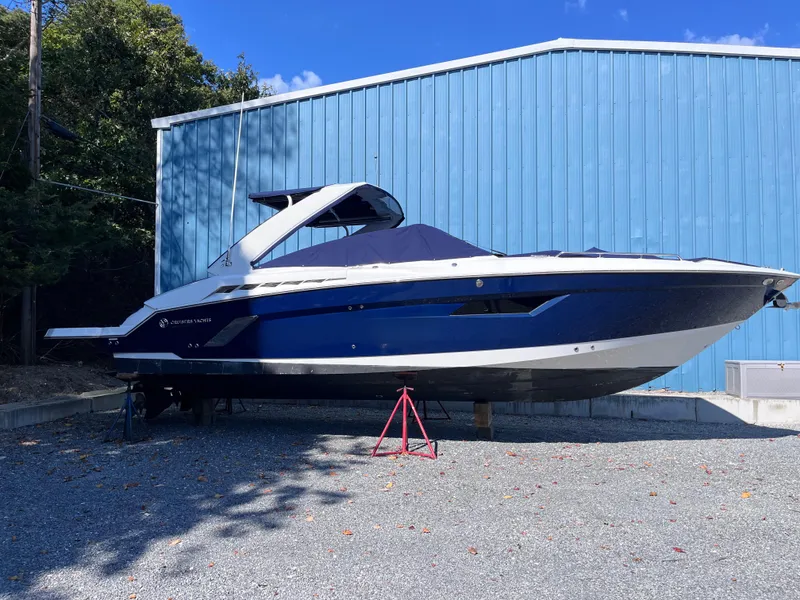 The Image of 2021 Cruisers Yachts 338 CX IO boat on gravel, blue building background. - 0