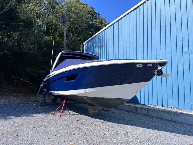 Slide: The Image of 2021 Cruisers Yachts 338 CX IO boat on stands beside a blue building. - 2