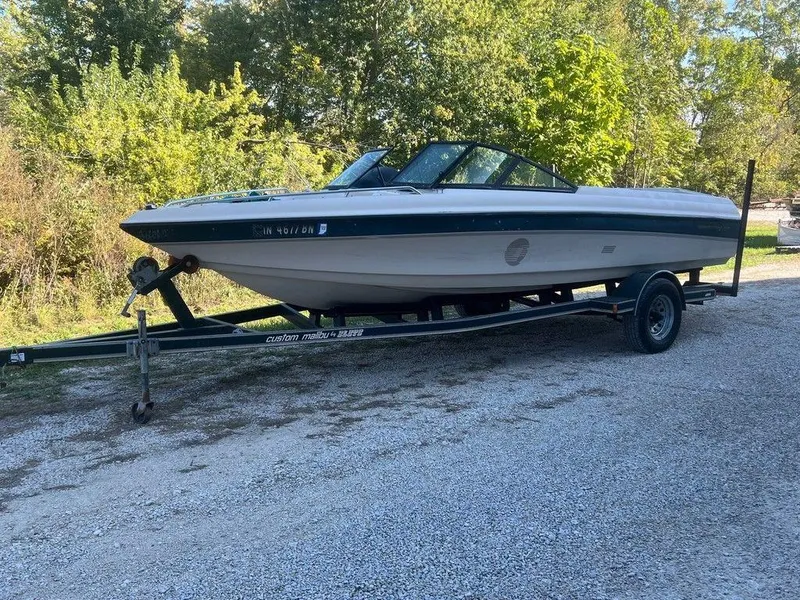 Slide: The Image of 1999 Malibu Sunsetter VLX boat on trailer, parked on gravel, surrounded by trees. - 1