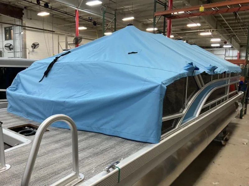 Slide: The Image of 2025 Bennington 22SLJ pontoon boat with blue cover in a warehouse setting. - 11