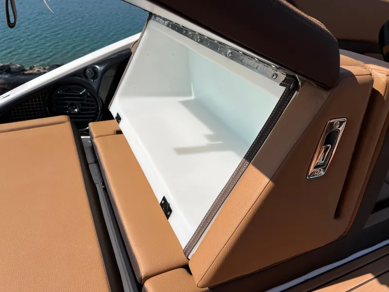 Slide: The Image of 2025 Yamaha Boats 252SD storage compartment with tan upholstery, open by the water. - 32