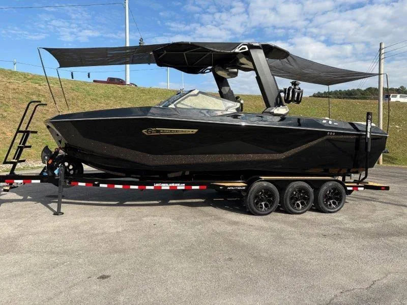 Slide: The Image of 2025 Nautique G25 boat on trailer, black exterior, parked outdoors under blue sky. - 119