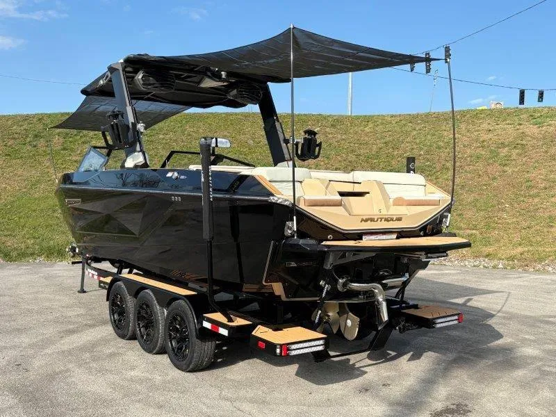 Slide: The Image of 2025 Nautique G25 boat on trailer, black exterior, beige interior, parked outdoors. - 120