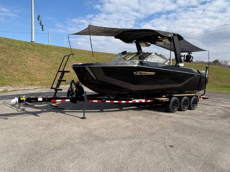 Slide: The Image of 2025 Nautique G25 boat on trailer with canopy, parked outdoors. - 129
