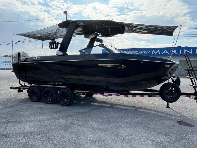 Slide: The Image of 2025 Nautique G25 boat on trailer at marina, under cloudy sky. - 130