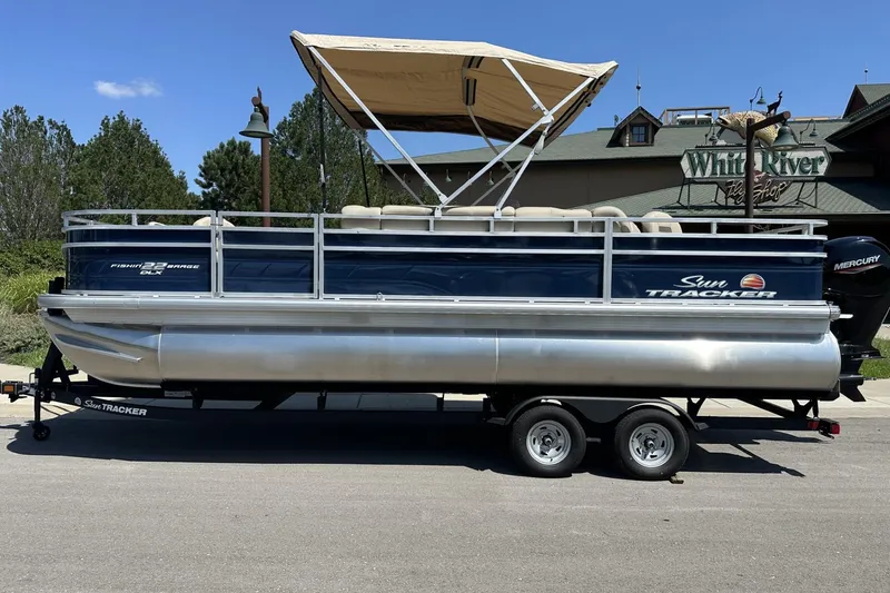 The Image of 2025 Sun Tracker Fishin' Barge 22 DLX pontoon boat with canopy on trailer. - 0