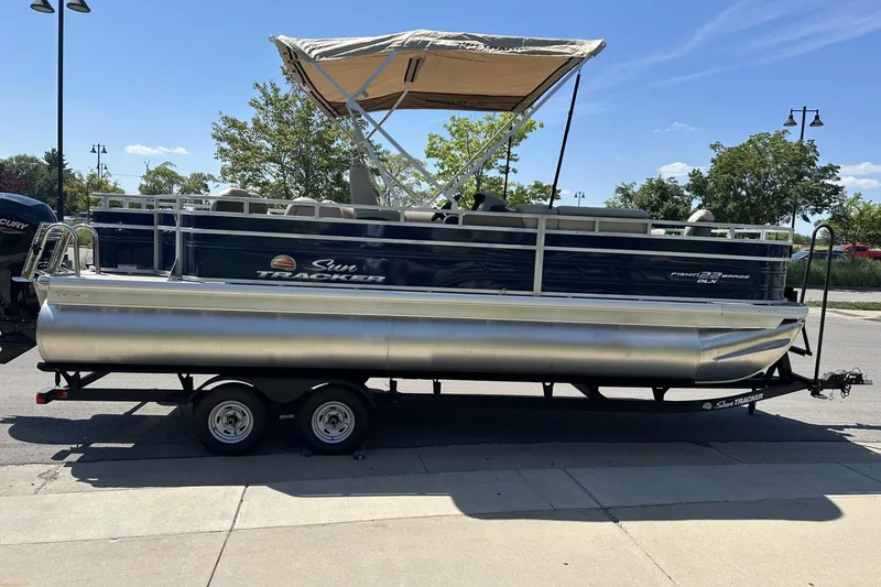 Slide: The Image of 2025 Sun Tracker Fishin' Barge 22 DLX pontoon boat on trailer, parked outdoors. - 6