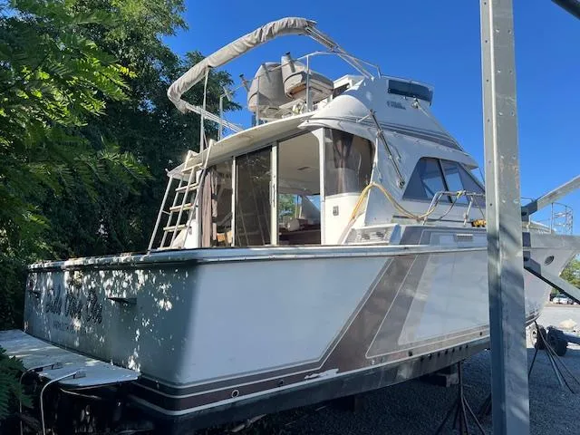 Slide: The Image of 1985 Trojan 11 Meter Express boat on land, surrounded by trees, under clear blue sky. - 2