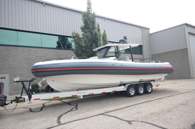 Slide: The Image of 2025 Zodiac X10CC boat with twin Mercury 400 engines on trailer, parked outside industrial building. - 1