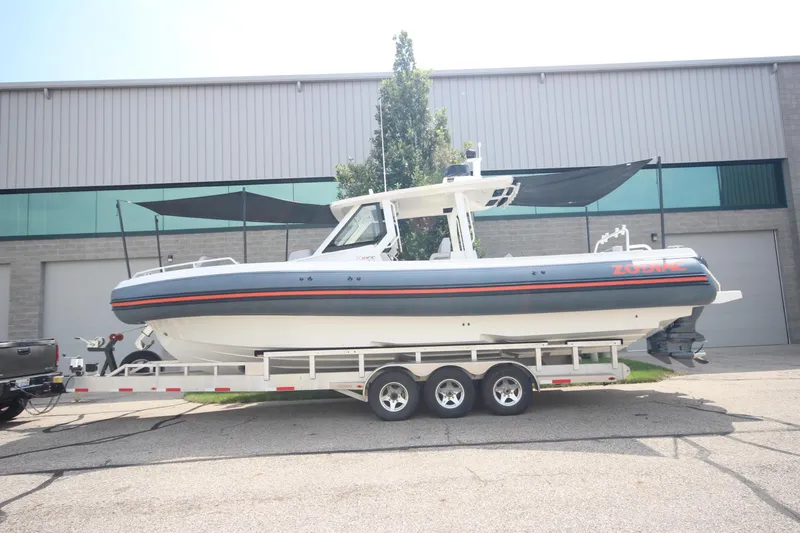 Slide: The Image of 2025 Zodiac X10CC boat with luxurious seating, parked on a trailer in an industrial area. - 38